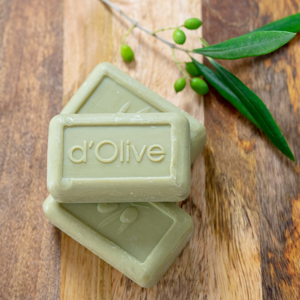 Three bars of d'Olive soap on a wooden surface.